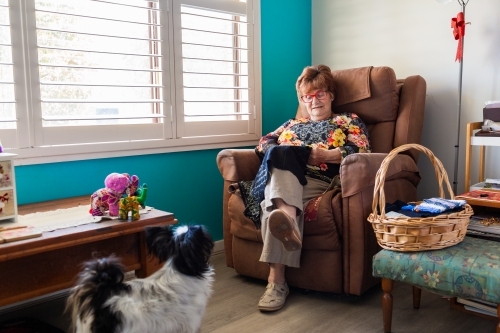 Senior woman sitting in chair doing needlework at home - Australian Stock Image