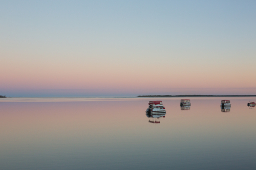 Serene twilight scene. Calm water mirrors pastel sky and small boats, peaceful, minimalist landscape - Australian Stock Image