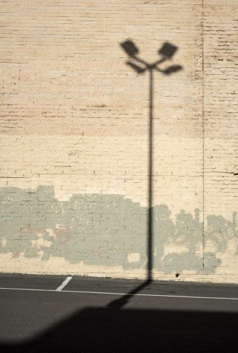 Shadow of a street lamp against a light brick wall - Australian Stock Image