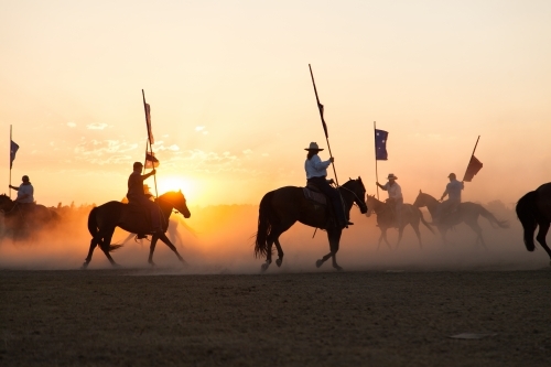 Shadows and silhouettes of horses and riders with australian flags on dust at sunset - Australian Stock Image