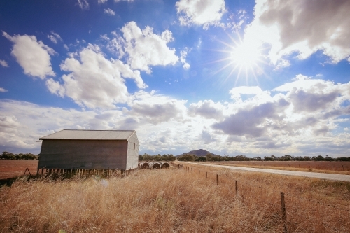 Shearing shed on country property surrounded by long dry grass under a cloudy sky - Australian Stock Image