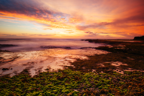 shoreline of Pearses Beach and headland around Pirates Bay Cove on a hot summer's evening - Australian Stock Image