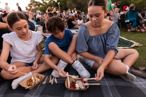 siblings sharing waffles on a picnic rug at the carols