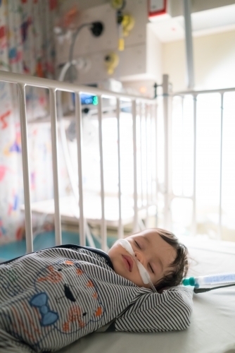 Sick mixed race year old boy asleep being treated with oxygen therapy in Children's Hospital ward - Australian Stock Image
