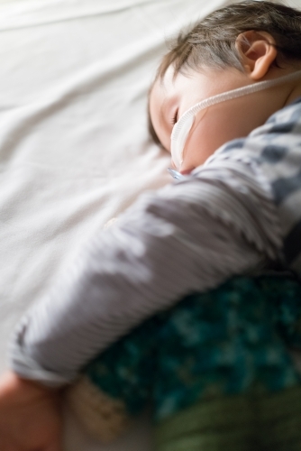 Sick mixed race year old boy asleep being treated with oxygen therapy in Children's Hospital ward - Australian Stock Image