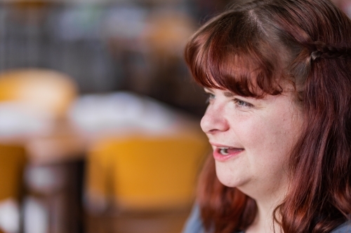 Side view of a young woman happily chatting with a friend at cafe - Australian Stock Image