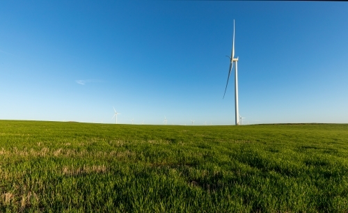 side view of wind turbine in farmland against blue sky - Australian Stock Image