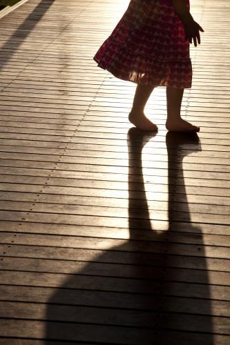 Silhouette and shadow of a young girl's legs standing on a merbau deck - Australian Stock Image