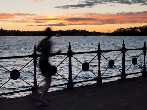 Silhouette of blurred runner on the edge of Sydney Harbour at sunset - Australian Stock Image