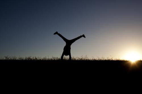 Silhouette of girl doing a cartwheel at sunset - Australian Stock Image