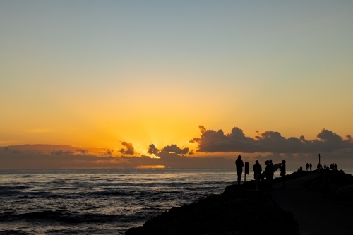 Silhouette of group of people gathering to watch the sunrise from the breakwall at Brunswick Heads - Australian Stock Image