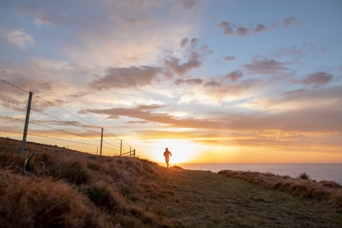 Silhouette of Man in Distance Running Towards Sunrise - Australian Stock Image