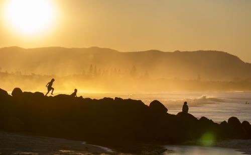 Silhouette of people walking over rocks near the ocean - Australian Stock Image