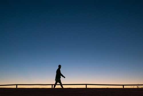 Silhouette of person walking along walkway at dawn. - Australian Stock Image