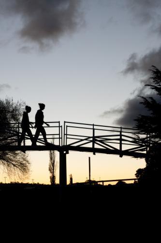 Silhouette of two people walking across a bridge - Australian Stock Image