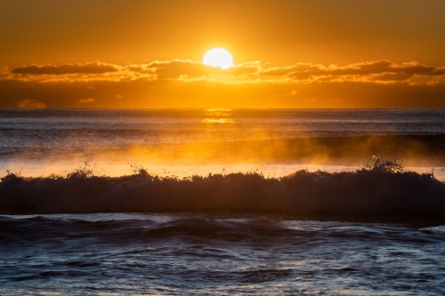 silhouette shot of big waves in the ocean at sunrise - Australian Stock Image