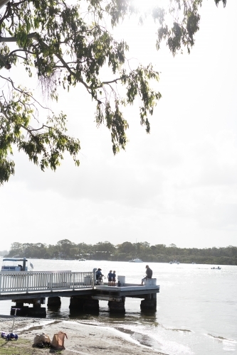silhouettes of men and children fishing off a jetty in the afternoon - Australian Stock Image