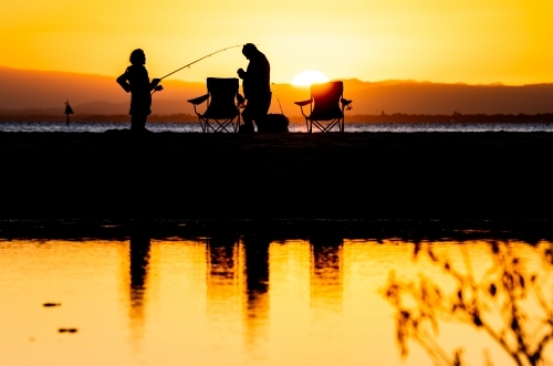 silhouettes of people fishing on the beach at sunset - Australian Stock Image