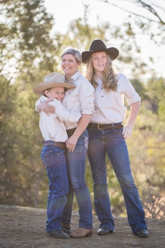 Single mother hugging son laughing with daughter standing behind on farm in drought - Australian Stock Image