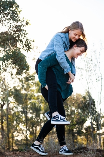 Sister giving her younger sibling a piggyback ride - Australian Stock Image