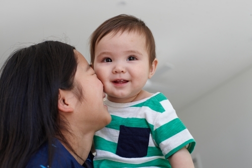 Sister holding younger baby brother in kitchen - Australian Stock Image