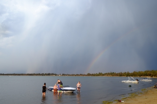 Skiing boat on lake at anchor with stormy skies and rainbow in the background - Australian Stock Image