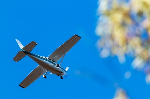 small aeroplane flying over against blue sky - Australian Stock Image