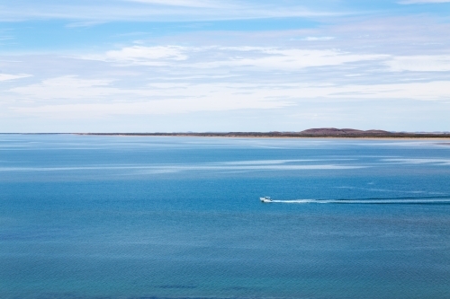 small boat heading out to sea across a calm bay - Australian Stock Image