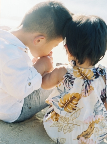 Small boy sitting down, kissing his sister's hand - Australian Stock Image
