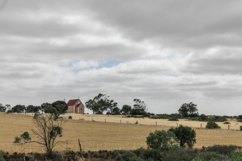 Small church on a hill with trees, fences and wheat