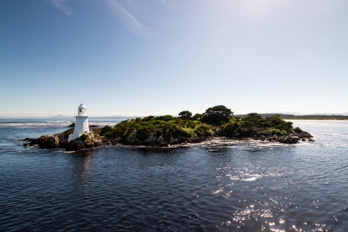 Small island with a cute little lighthouse, blue sky and bluewater. - Australian Stock Image