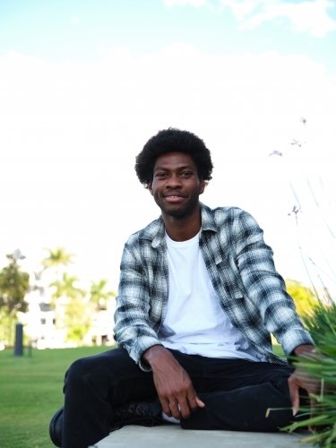 Smiling man sitting on a concrete park bench wearing a checkered polo shirt - Australian Stock Image