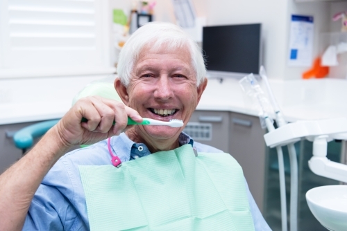 Smiling elderly man at dentist holding toothbrush - Australian Stock Image