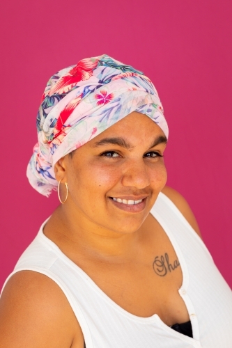 smiling indigenous woman wearing floral head wrap against pink background