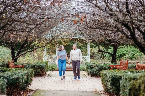 smiling lgbt  couple holding hands with dead trees, shrubs and wooden benches on the side - Australian Stock Image