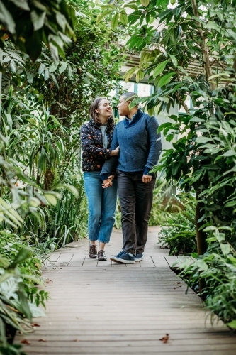 smiling lgbtqi couple holding hands while looking at each other walking in a garden - Australian Stock Image