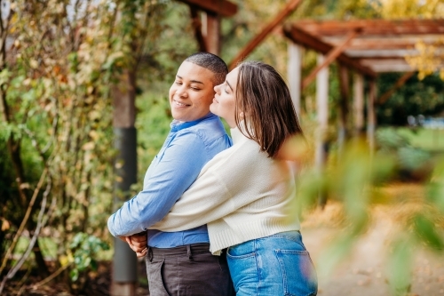 smiling lgbtqi couple hugging and kissing on the cheek - Australian Stock Image