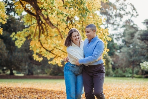 smiling lgbtqi couple hugging each other by the autumn trees - Australian Stock Image