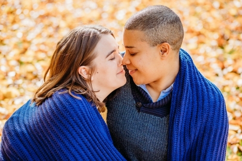 smiling lgbtqi couple looking at each other outside with blue blanket wrapped around them - Australian Stock Image