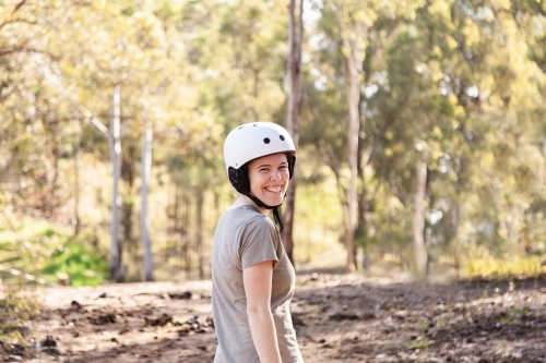 Smiling woman with horse riding helmet on looking back over her shoulder - Australian Stock Image