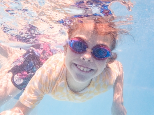 Smiling young Australian girl swimming in pool with goggles on in summer - Australian Stock Image
