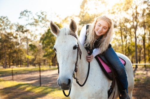 Smiling young teen lady sitting on her white horse in paddock - Australian Stock Image