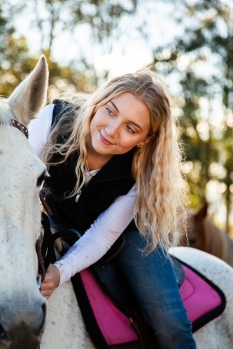 Smiling young teen lady sitting on her white horse in paddock - Australian Stock Image