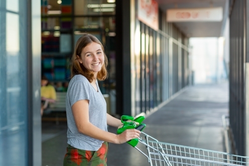 smiling young woman pushing shopping trolley at shops - Australian Stock Image