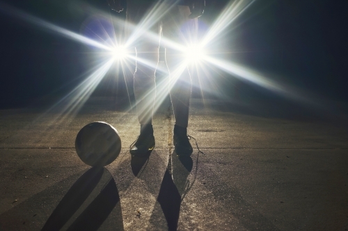Soccer player standing in front of headlights at night - Australian Stock Image