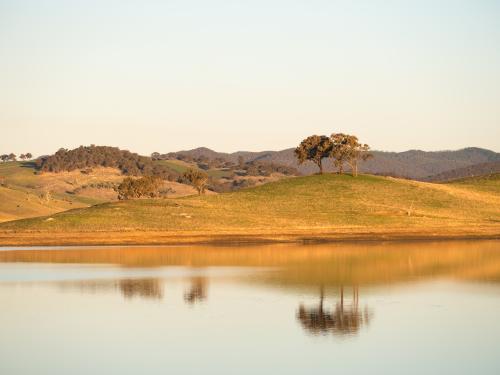 Soft reflection of hills and trees in a calm rural dam - Australian Stock Image