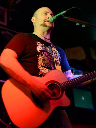 Solo entertainer singing and playing accoustic guitar with red lighting - Australian Stock Image