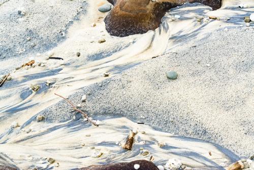 Speckled and streaked patterns in wet yellow and black mineral sands on a beach at low tide - Australian Stock Image