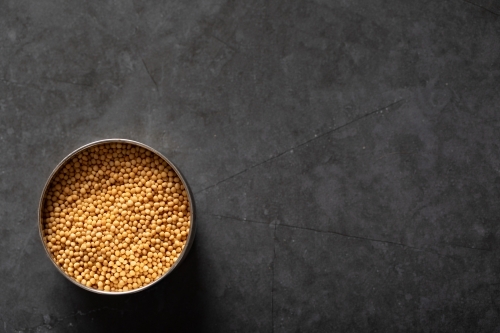 Spice tin of yellow mustards seeds on dark marble background - Australian Stock Image