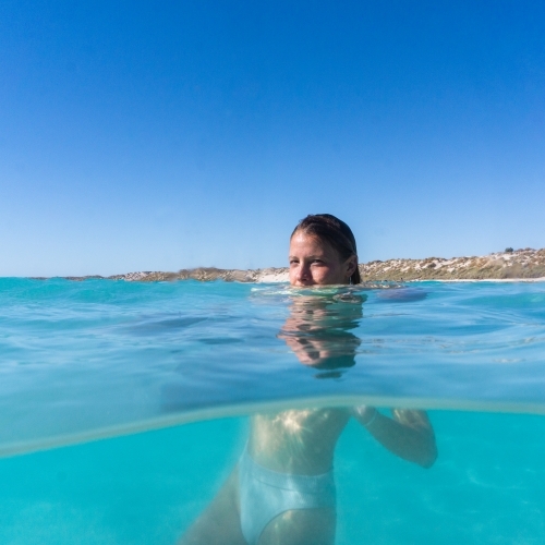 Split shot underwater view of woman floating in turquoise ocean with head above water - Australian Stock Image